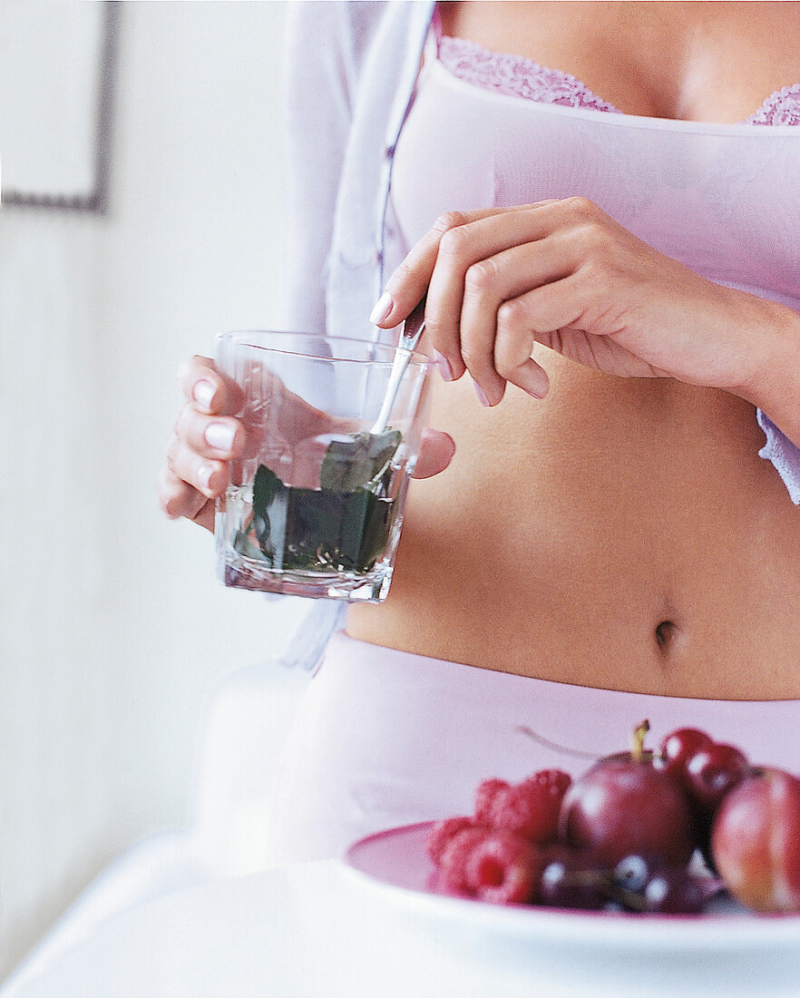 Frau in Wäsche mit einem  Glas mit Minze, Teller mit Obst, Früchte