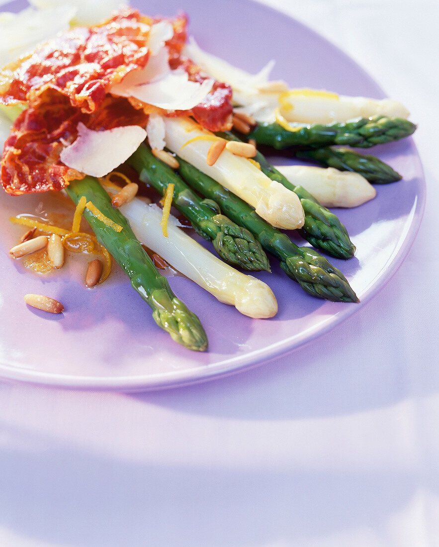 Close-up of white and green asparagus with ham, cheese and pine nuts on plate