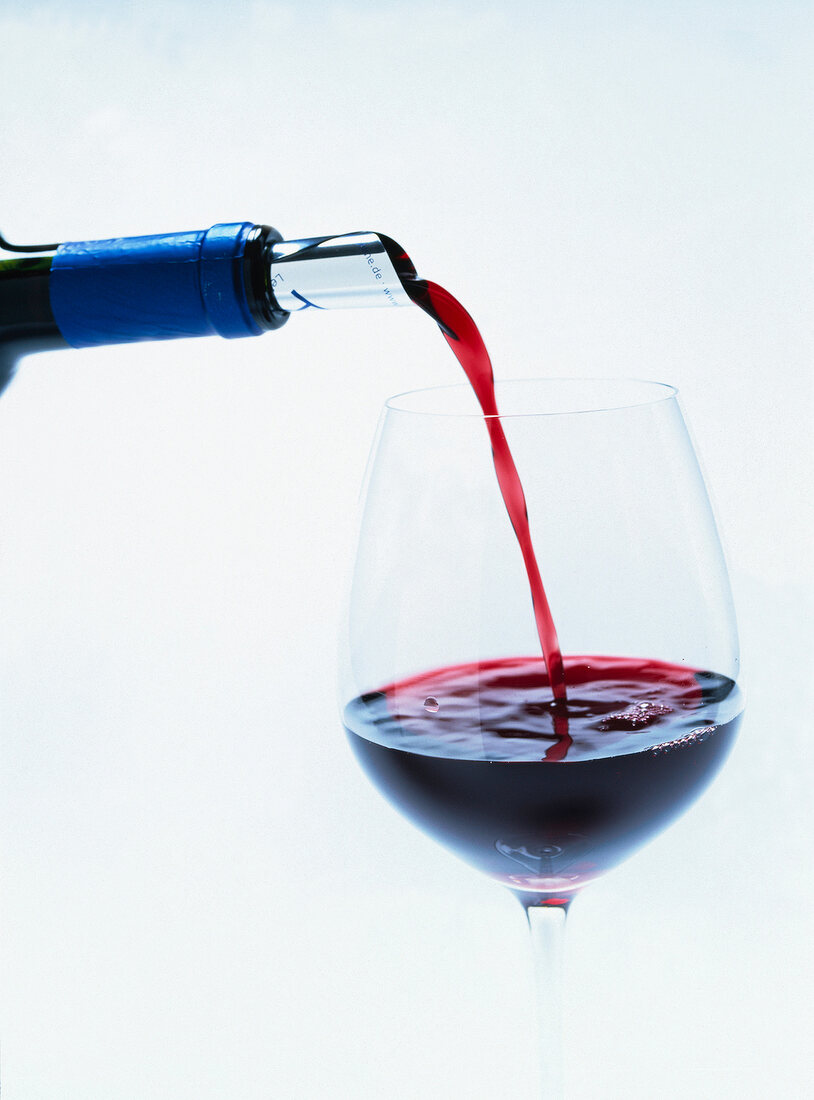 Close-up of red wine being poured in wine glass on white background
