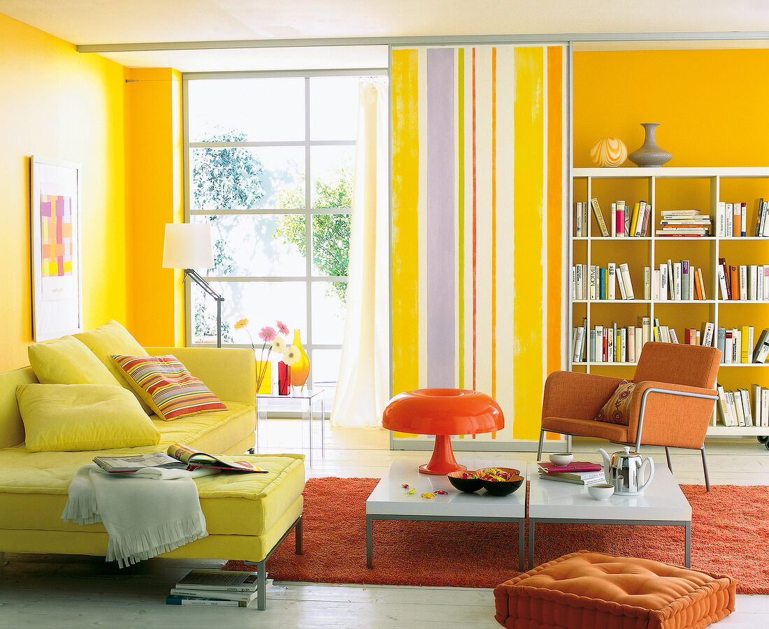 Living room with yellow walls, colourful furnishings, bookcase and sofa