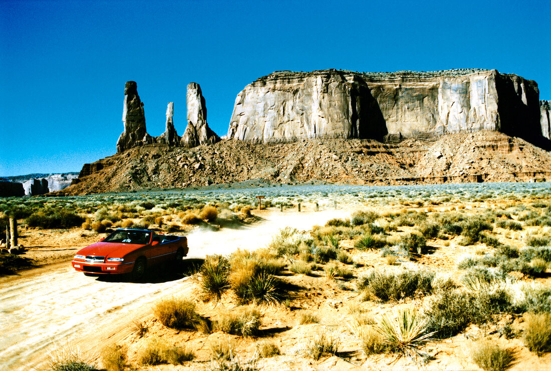 Red car passing through Monument Valley, Utah, USA