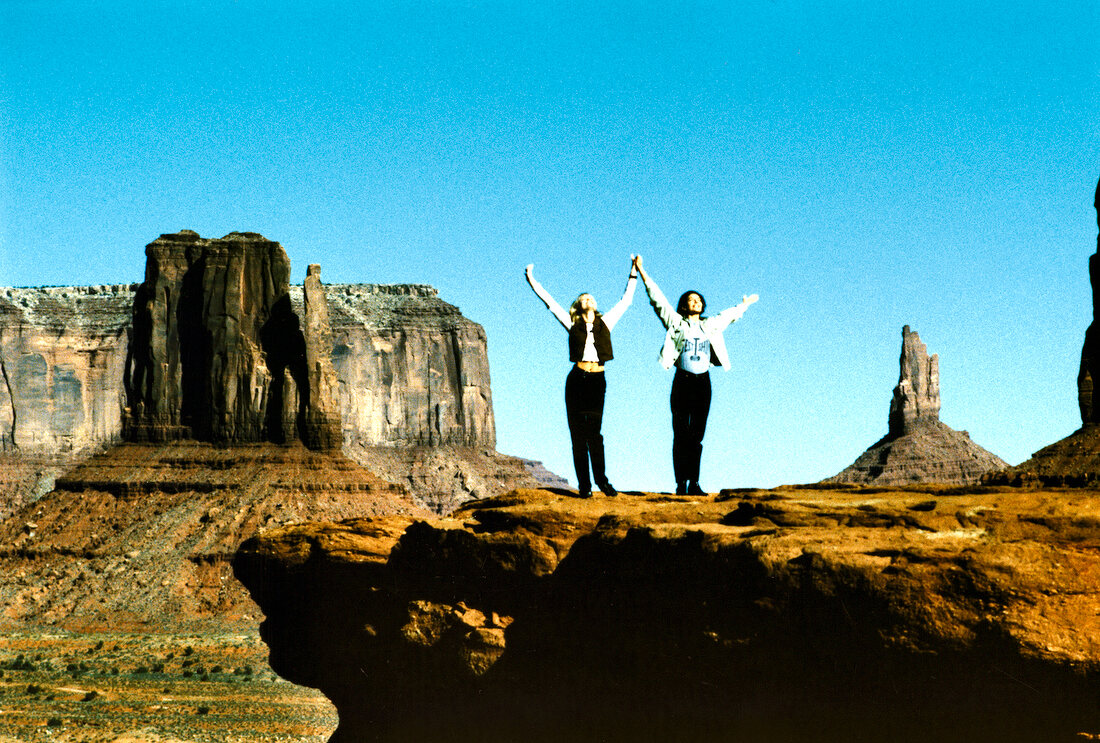 Two women standing on ledge of cliff, screaming with arms raised
