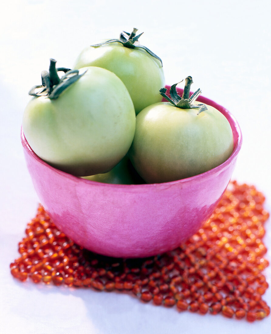 Close-up of green tomatoes in pink bowl on white background