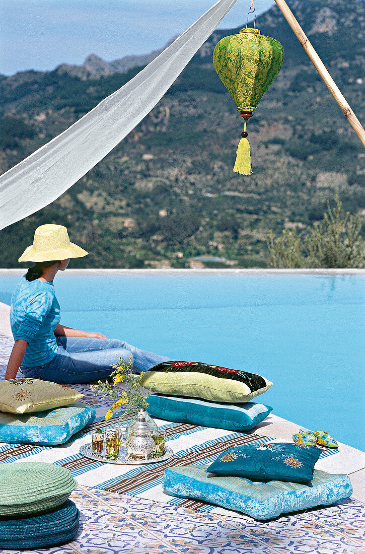 Rear view of woman wearing blue top and hat sitting under awning and looking at view