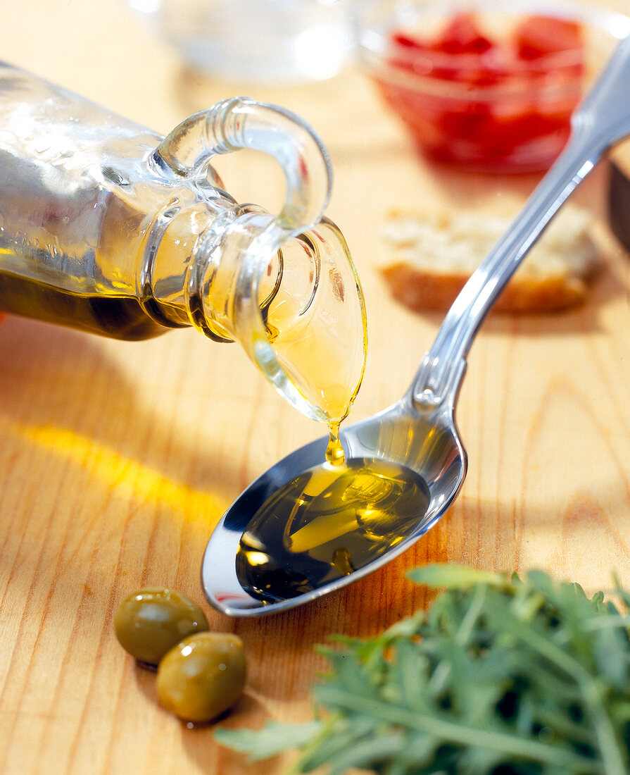 Olivenöl wird aus einer Flasche auf einen Löffel gegossen