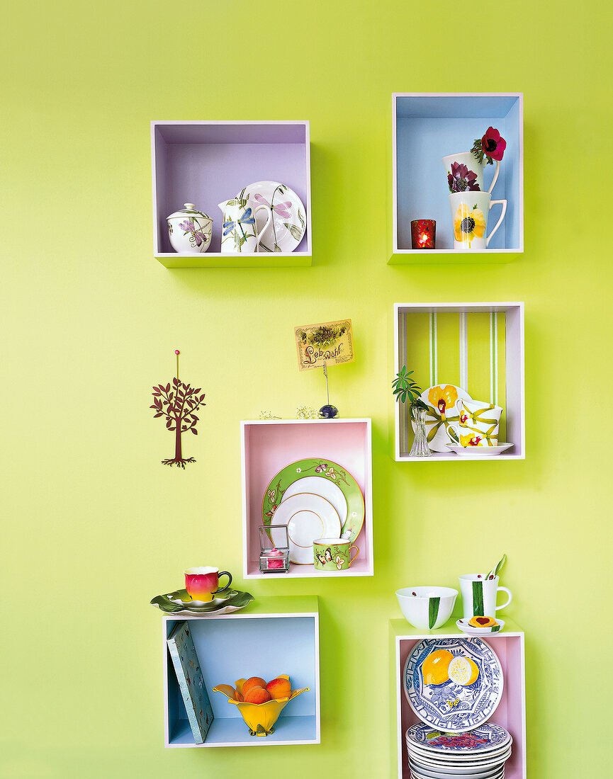 Shelf with porcelain crockery against green painted wall