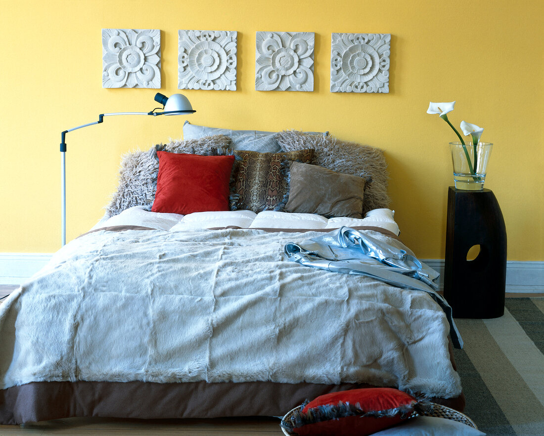 Bed with pillows decorated with patterned tiles on yellow wall