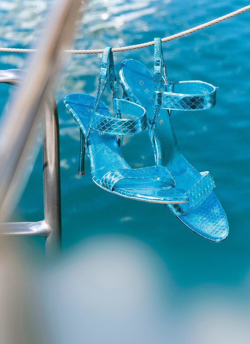 Pair of turquoise high heel shoes hanging on rope above swimming pool
