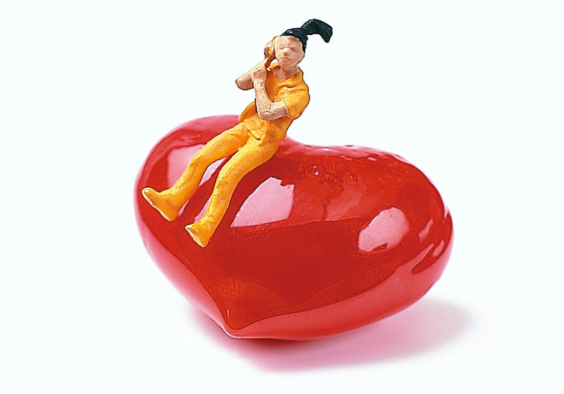 Spielzeugfigur auf rotem Herz mit Telefon in der Hand, Freisteller