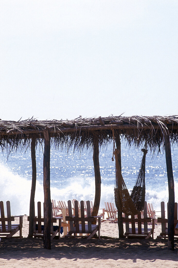 Stühle am Strand von Acapulco unter Sonnenschutz aus Palmwedeln