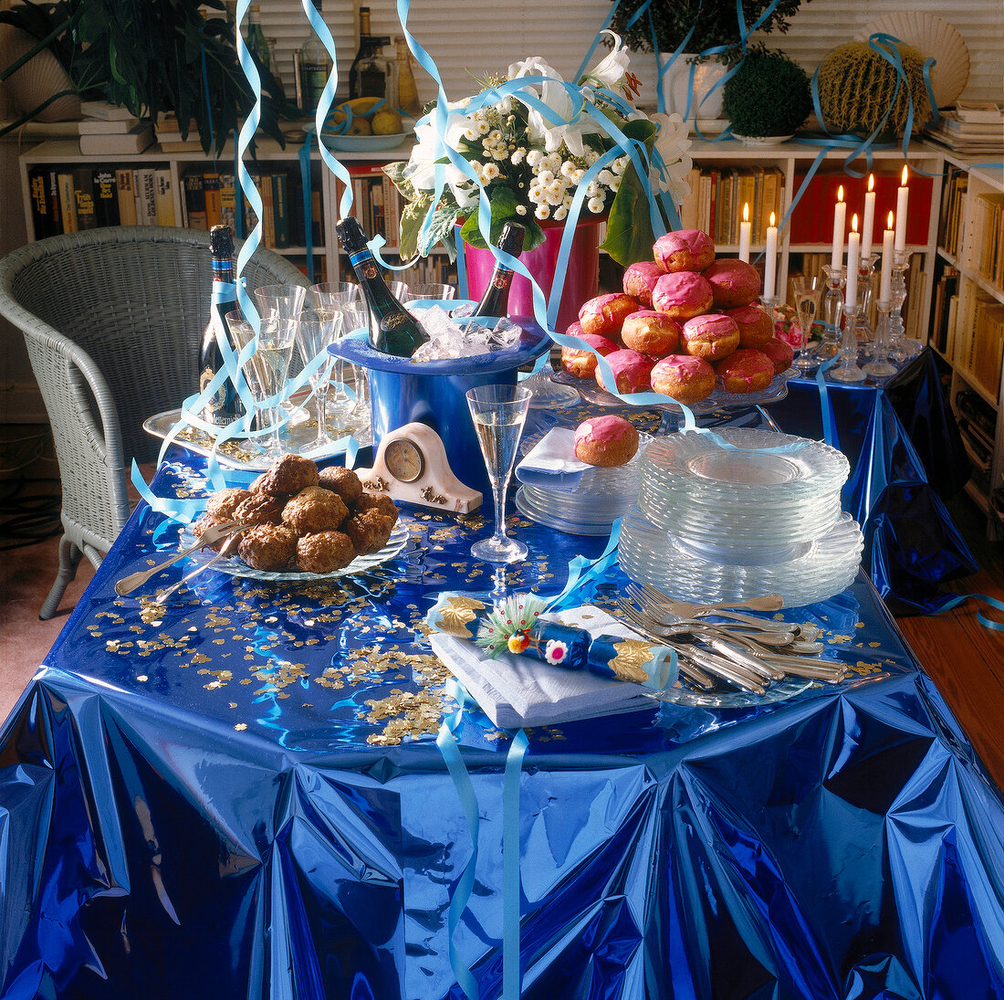Silvestertisch mit blauer glänzender Tischdecke, Blumen, Konfetti, Essen