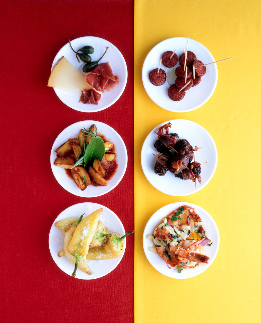 Six plates of appetizers such as patatas bravas, cheese and ham, chorizo, dates and bacon