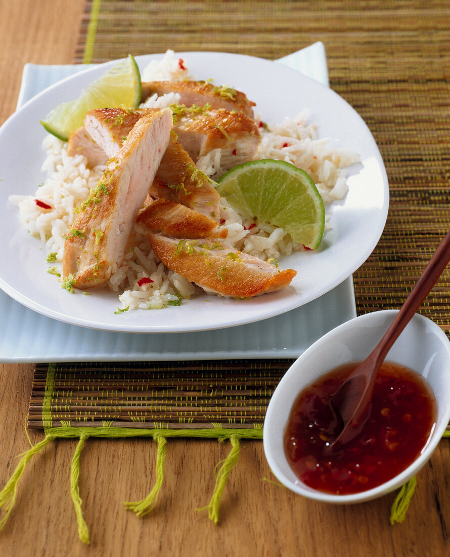 Chicken with coconut rice, lime juice and chili on plate and bowl