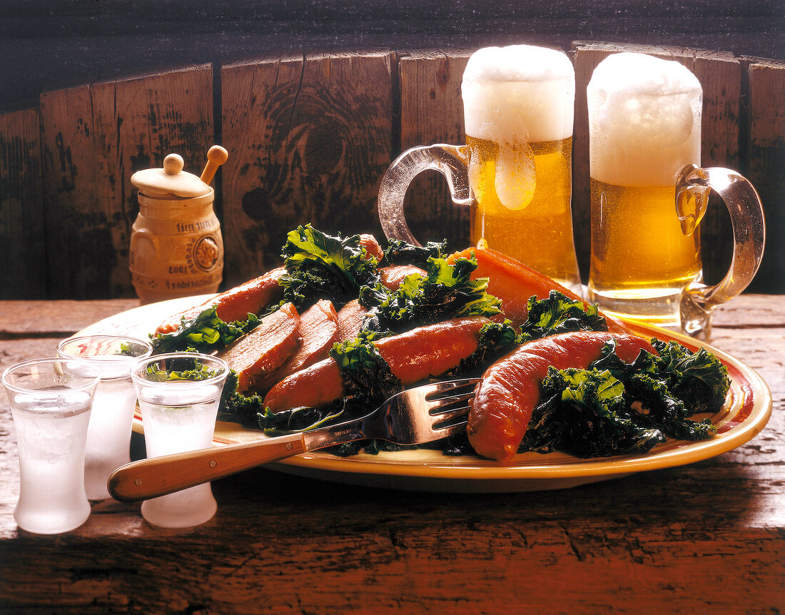 Kale with cooked sausage and glasses of beer on plate