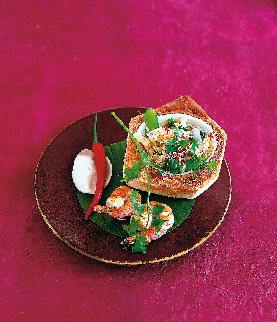 Asian salad in hollowed out coconut beside prawns and chili on banana leaf