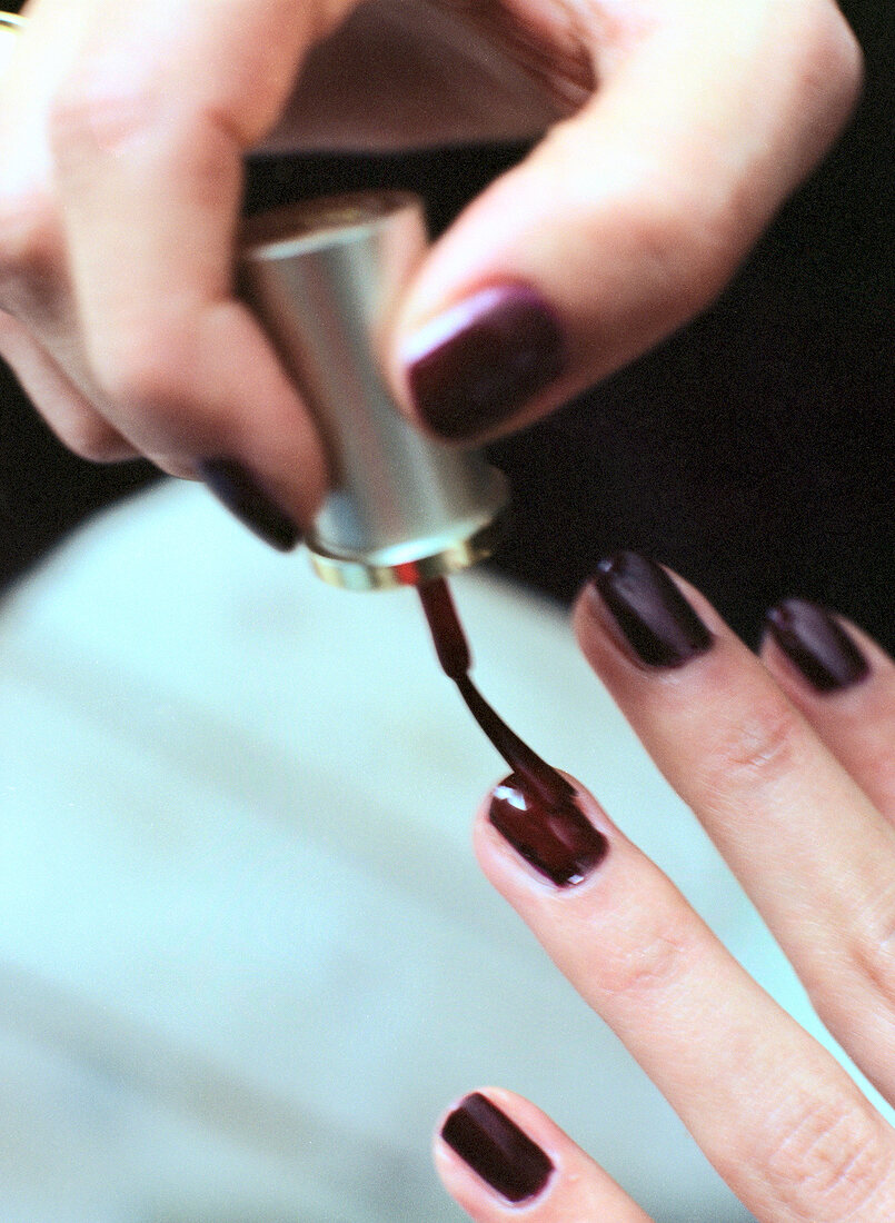 Close-up of woman's hands applying dark brown nail polish on finger nails