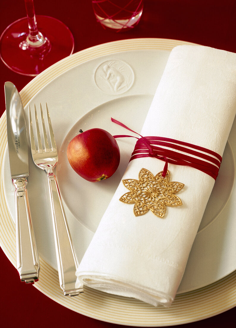 Napkin wrapped with red ribbon and apple on plate