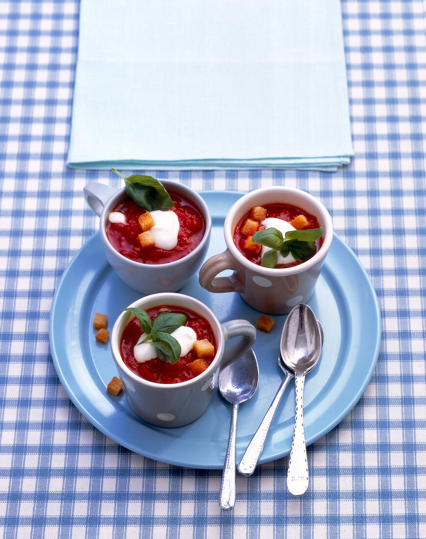 Three cup of tomato soup with cream and croutons on plate