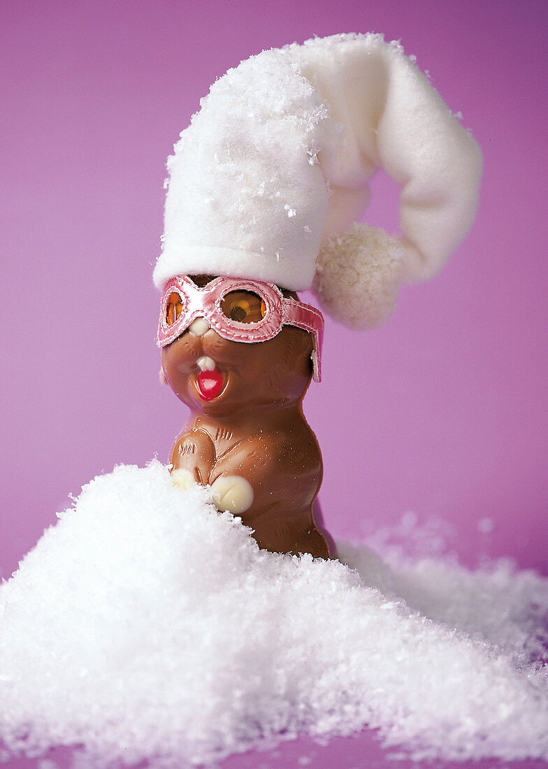 Schoko - Hase mit weißer Mütze und rosa Brille im Deko- Schnee