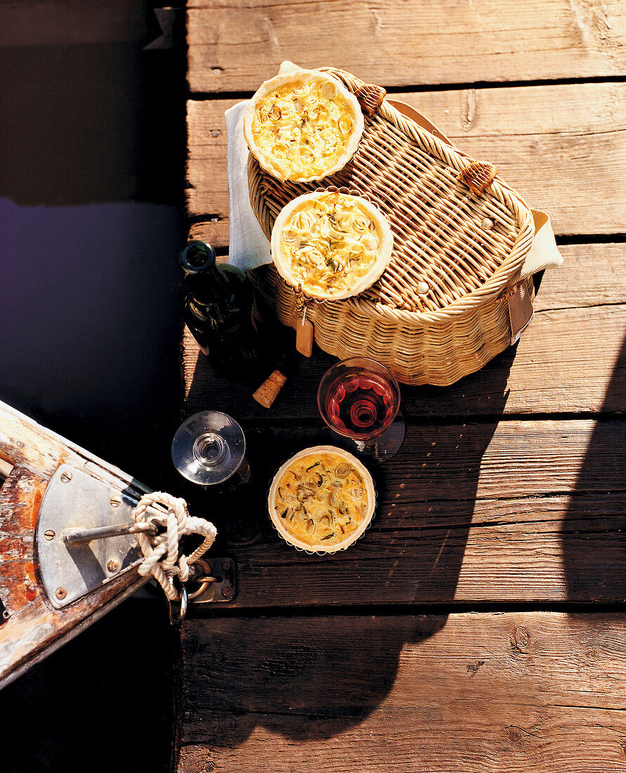 Quiche on picnic basket and wine glasses and bottle on jetty