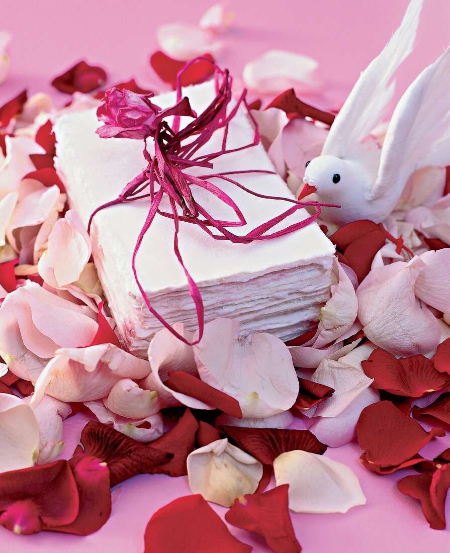 Bundled of handmade paper wrapped with red ribbon, toy bird and rose petals