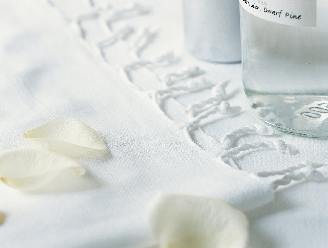 Close-up of towel with rose petals and bottles on white background