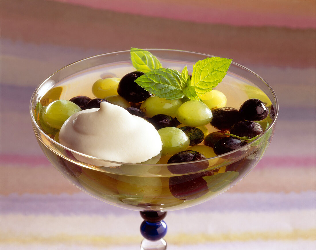 Close-up of green and blue grapes in jelly with coconut cream in glass