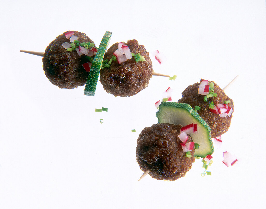 Close-up of hack skewers with zucchini, radishes and chives on white background