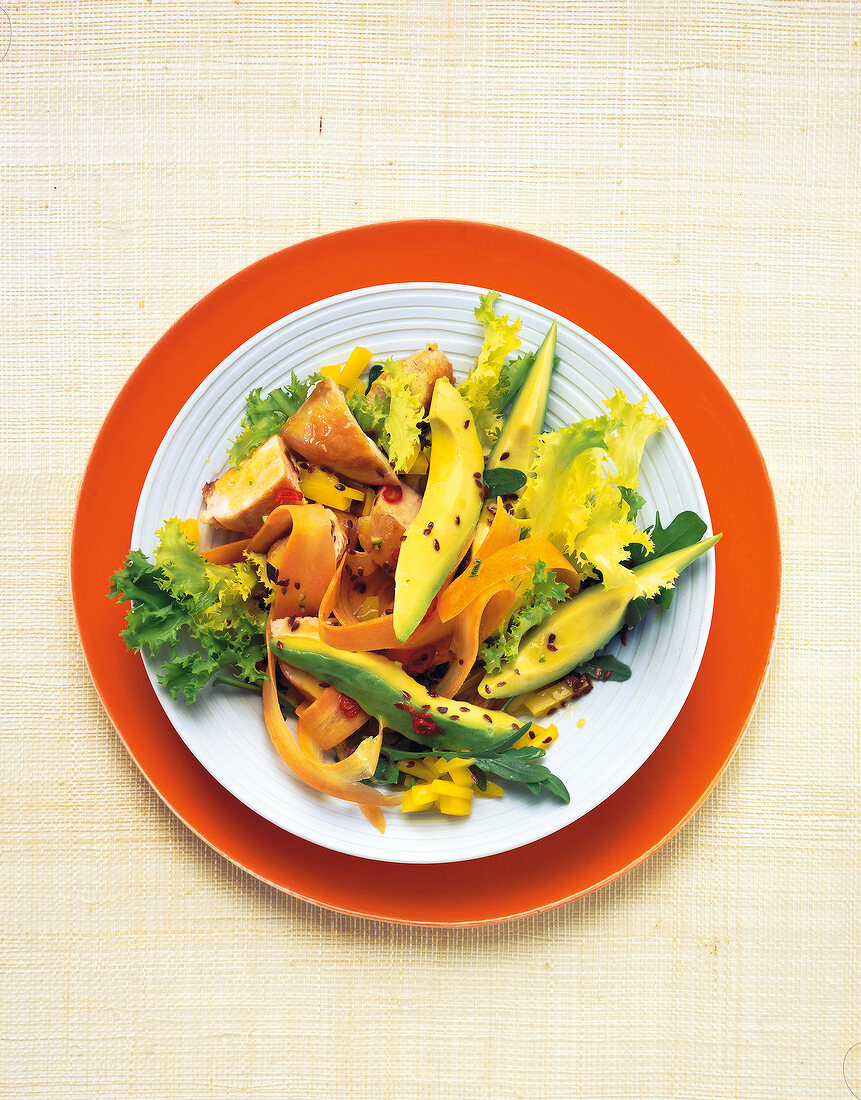 Bowl of avocado salad with chicken breast on orange plate, overhead view