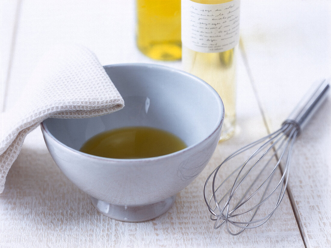Close-up of olive oil in bowl, napkin and whisk wire on wooden table