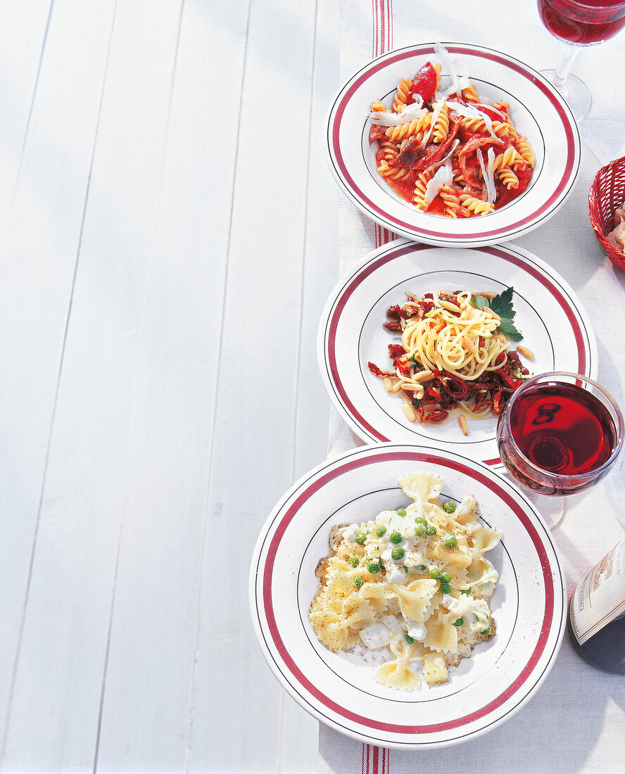 Three plates with pasta fusilli, farfalle and spaghetti with red wine glass