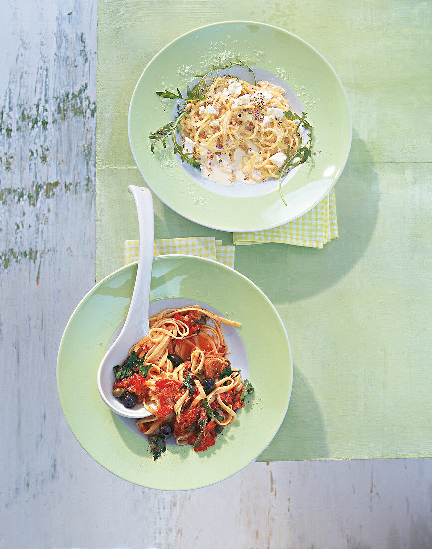 Two green plates each with a spaghetti pasta and bavette pasta on green table