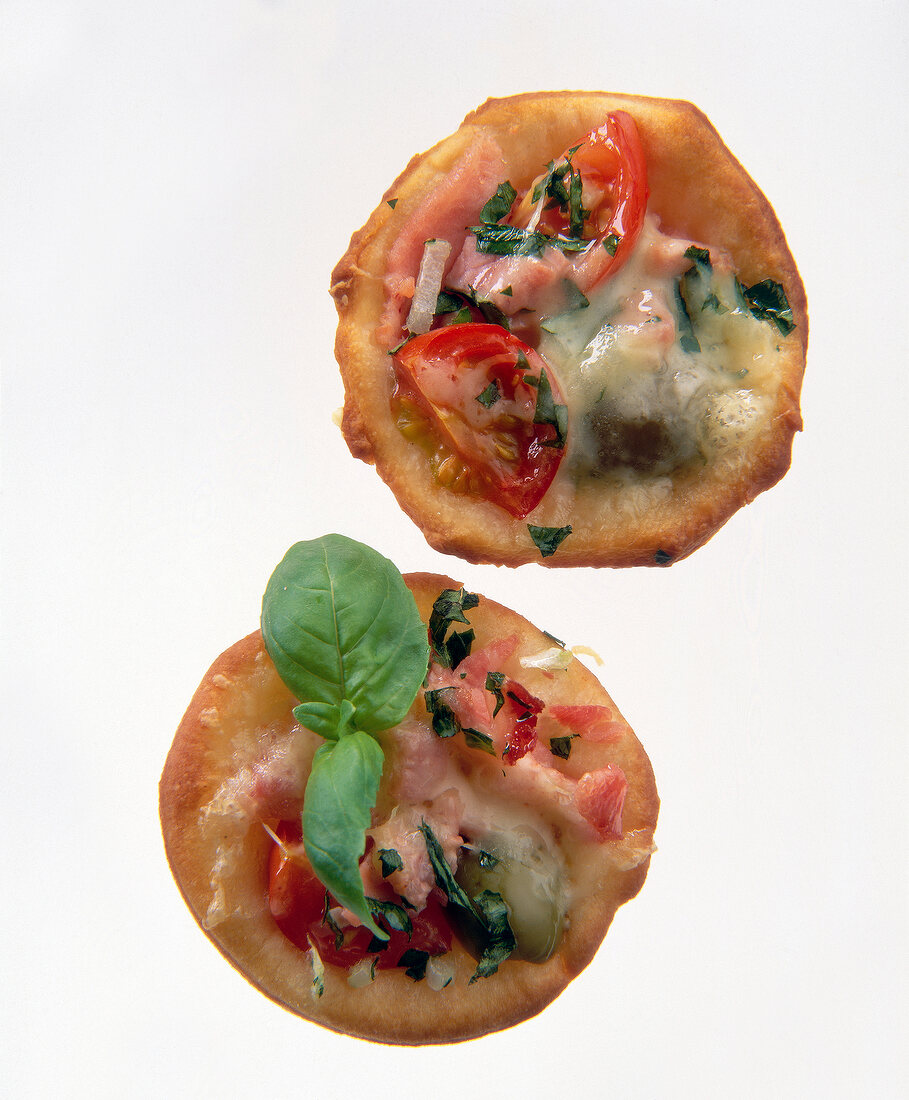 Close-up of small pizza with tomatoes, olives, ham and cheese on white background