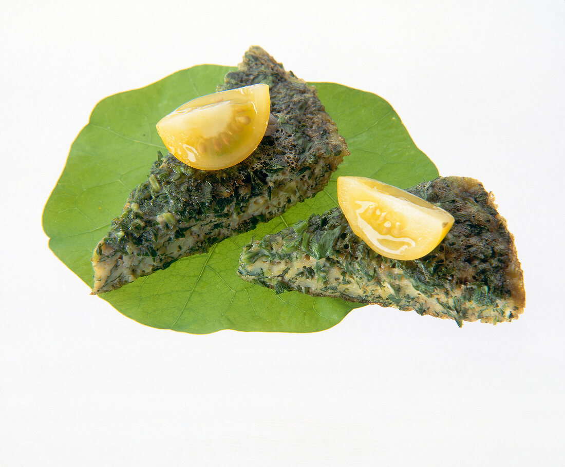 Close-up of yellow tomatoes on omelets with herbs and cheese on white background