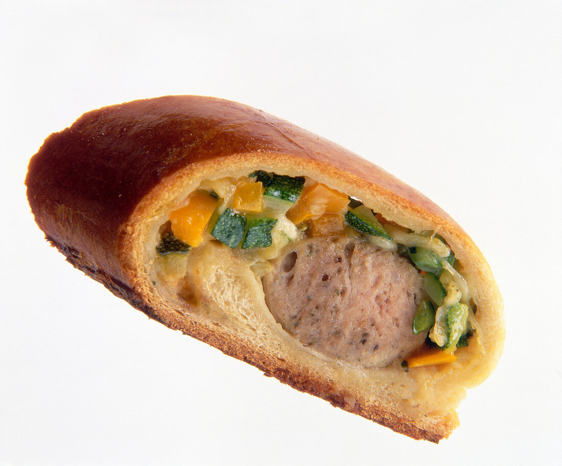 Close-up of sausage roll with carrots, zucchini and gouda on white background