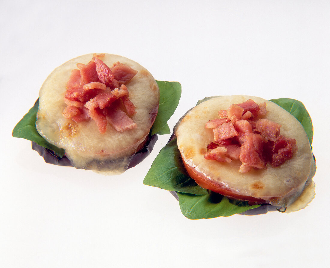 Eggplant topped with tomato, mozzarella and ham on white background