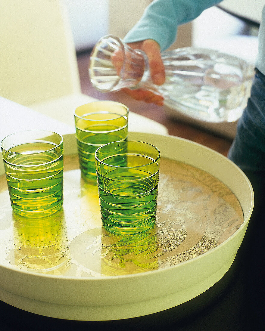 Drei grüne Gläser auf einem Tablett, Karaffe, Wasser einschenken