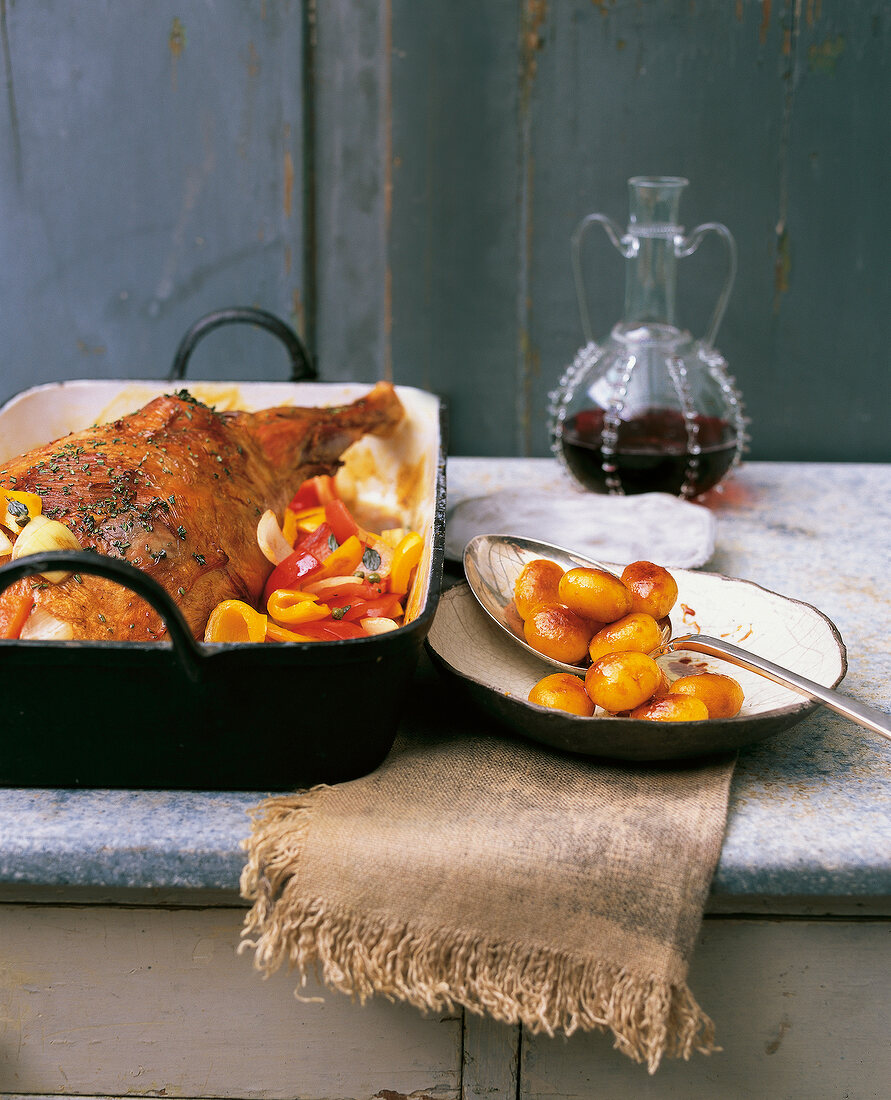 Roasted leg of lamb in gratin dish with bowl and carafe on table