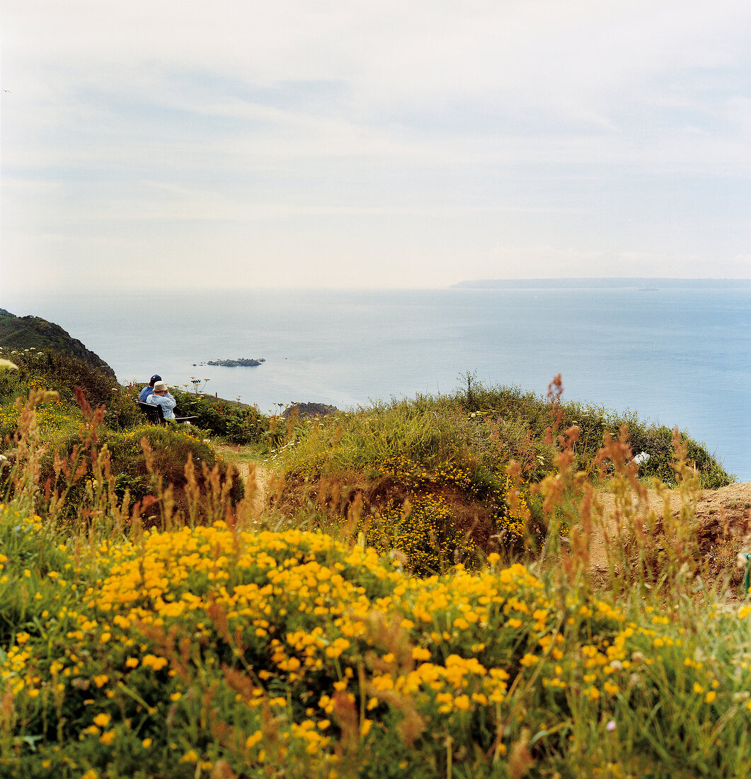 View of sea through cliffs with people sitting on park bench
