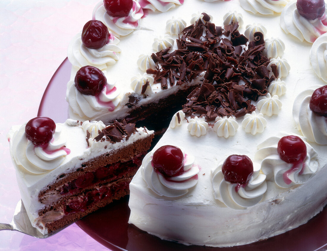 Cherry and chocolate gateau with one piece on spatula