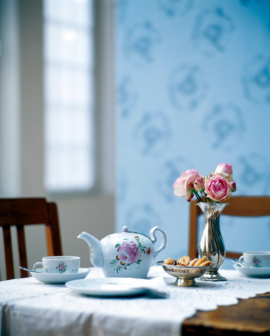 Tea set with rose motif and rose vase on wooden table