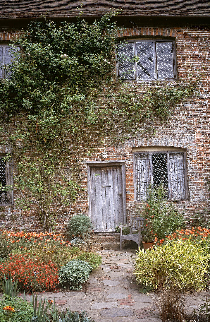 Entrance of country house with red flowers in front, Great Dixter