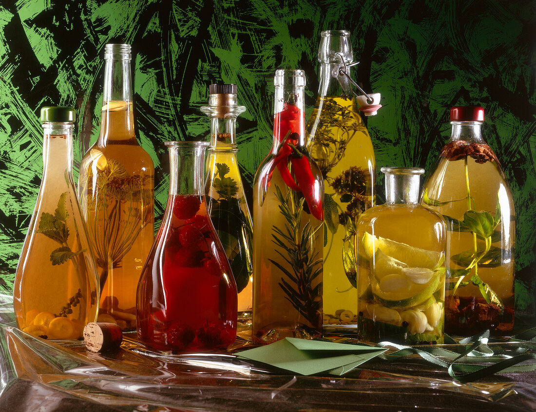 Different bottles with vinegar and herbs on table