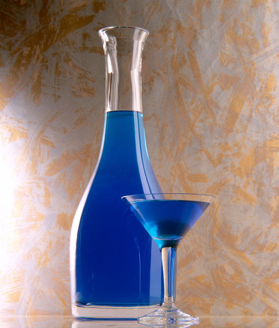 Karaffe Litschilikör aus Blue Curacao, davor Cocktailglas