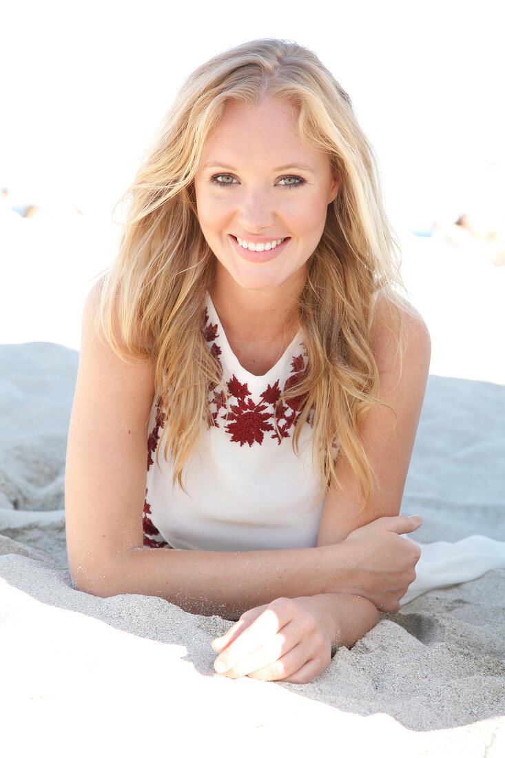 Blonde woman in a bright dress on the beach, smiling at the camera