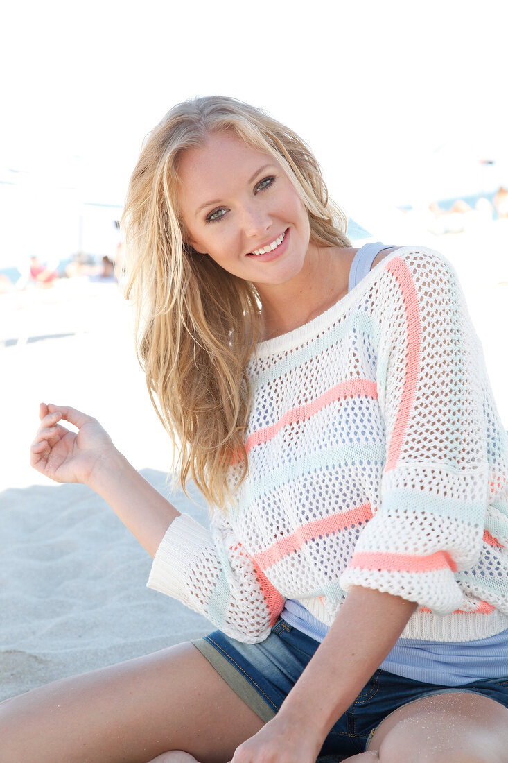 Blonde woman in a white sweater on the beach, smiling at camera