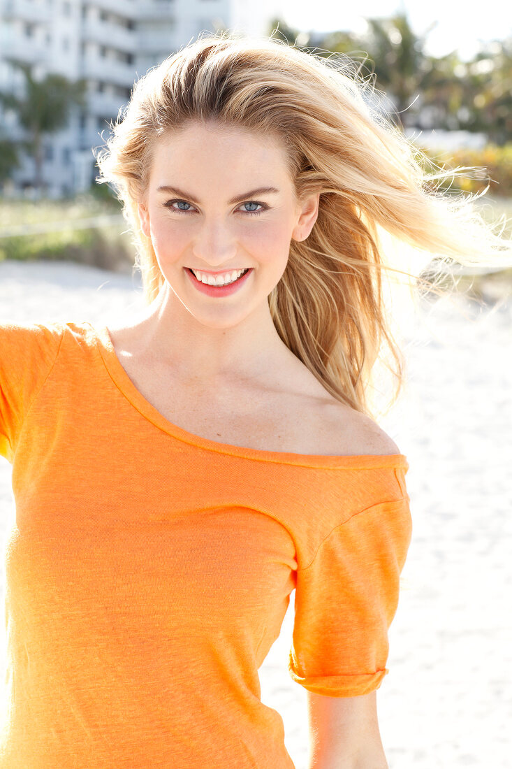 Blonde Frau mit langen Haaren in orangefarbenem T-Shirt am Strand