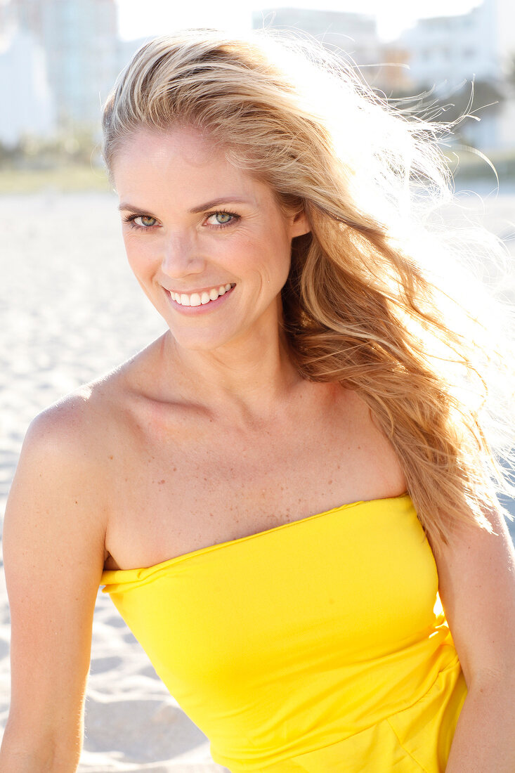 Blonde Frau mit langen Haaren im gelben Kleid am Strand