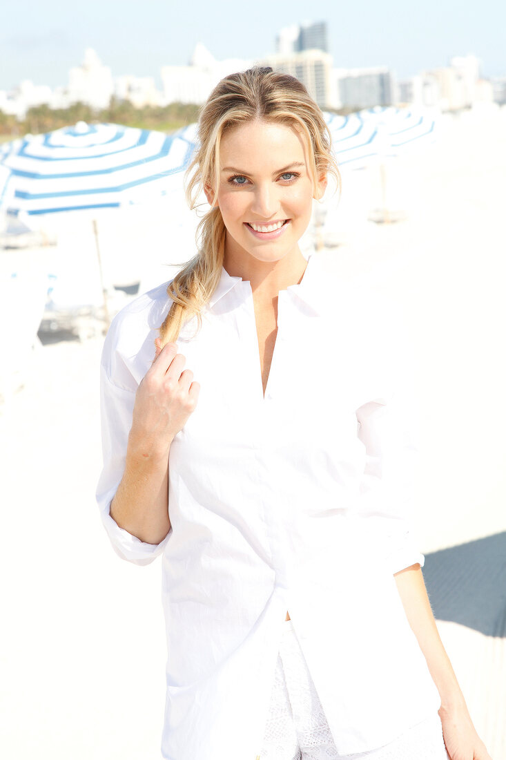 Blonde, sportliche Frau mit langen Haaren in weißer Bluse am Strand
