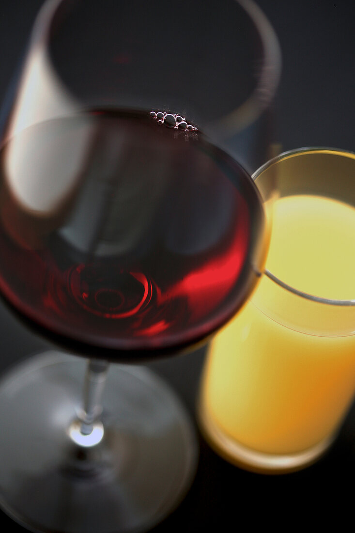 A glass of red wine next to a glass of orange juice